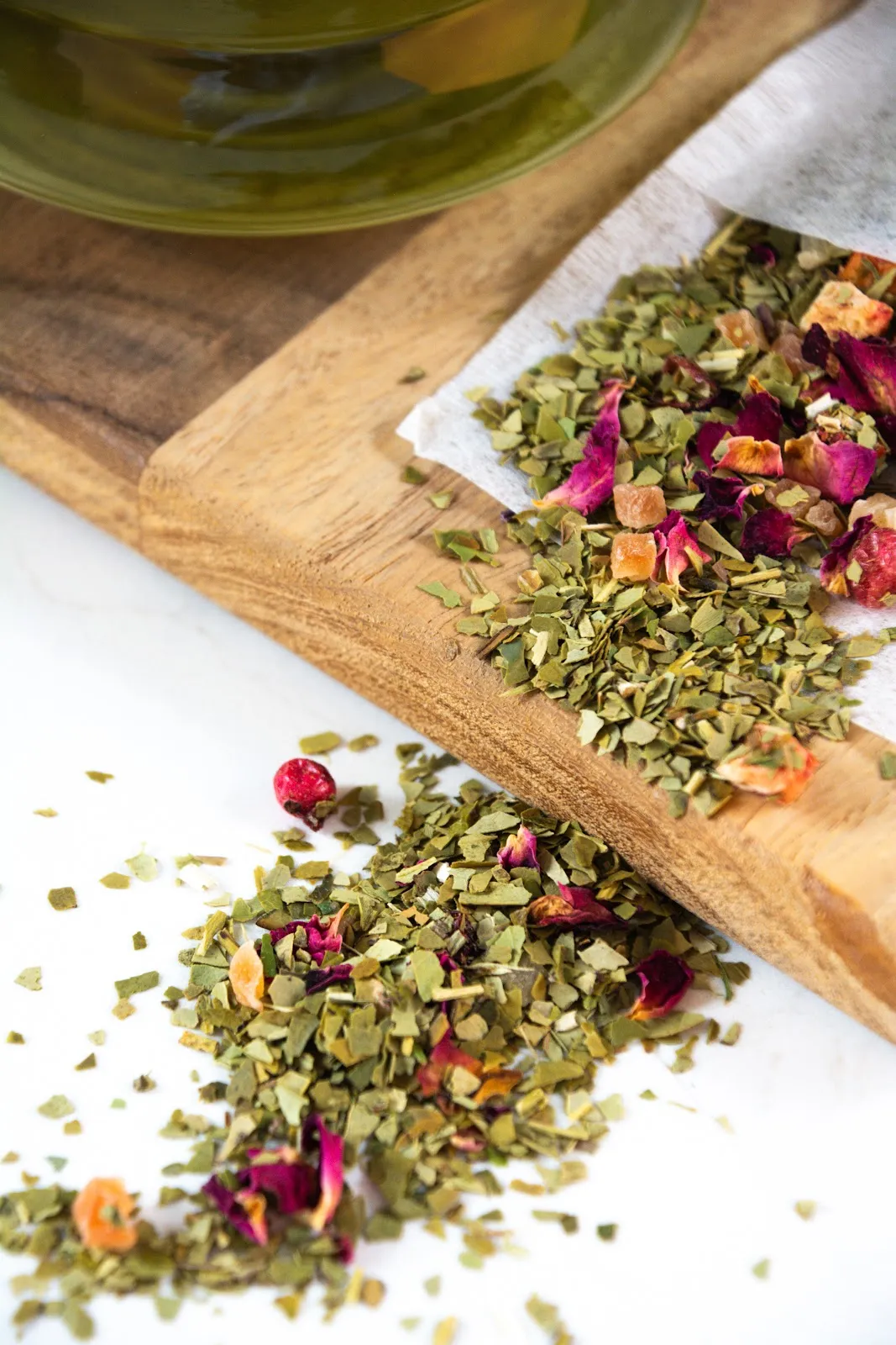 Losse yerba mate met rozenblaadjes op een houten plank naast een glazen kan mate